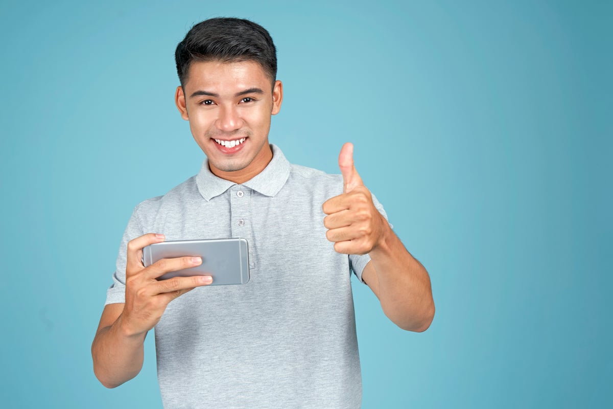 Man Gesturing Thumb Up with Smartphone  on Blue Background